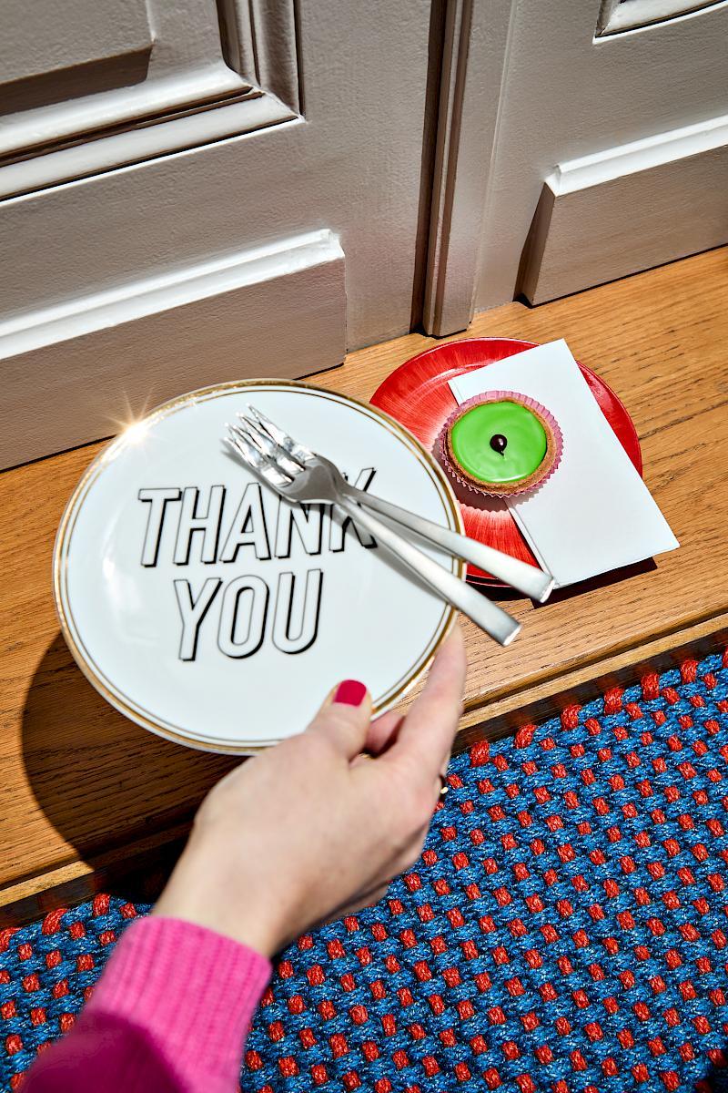 A woman's hand holding a Bitossi Home Thank you plate near a Serax Dé off-white/red plate in front of a hay door mat
