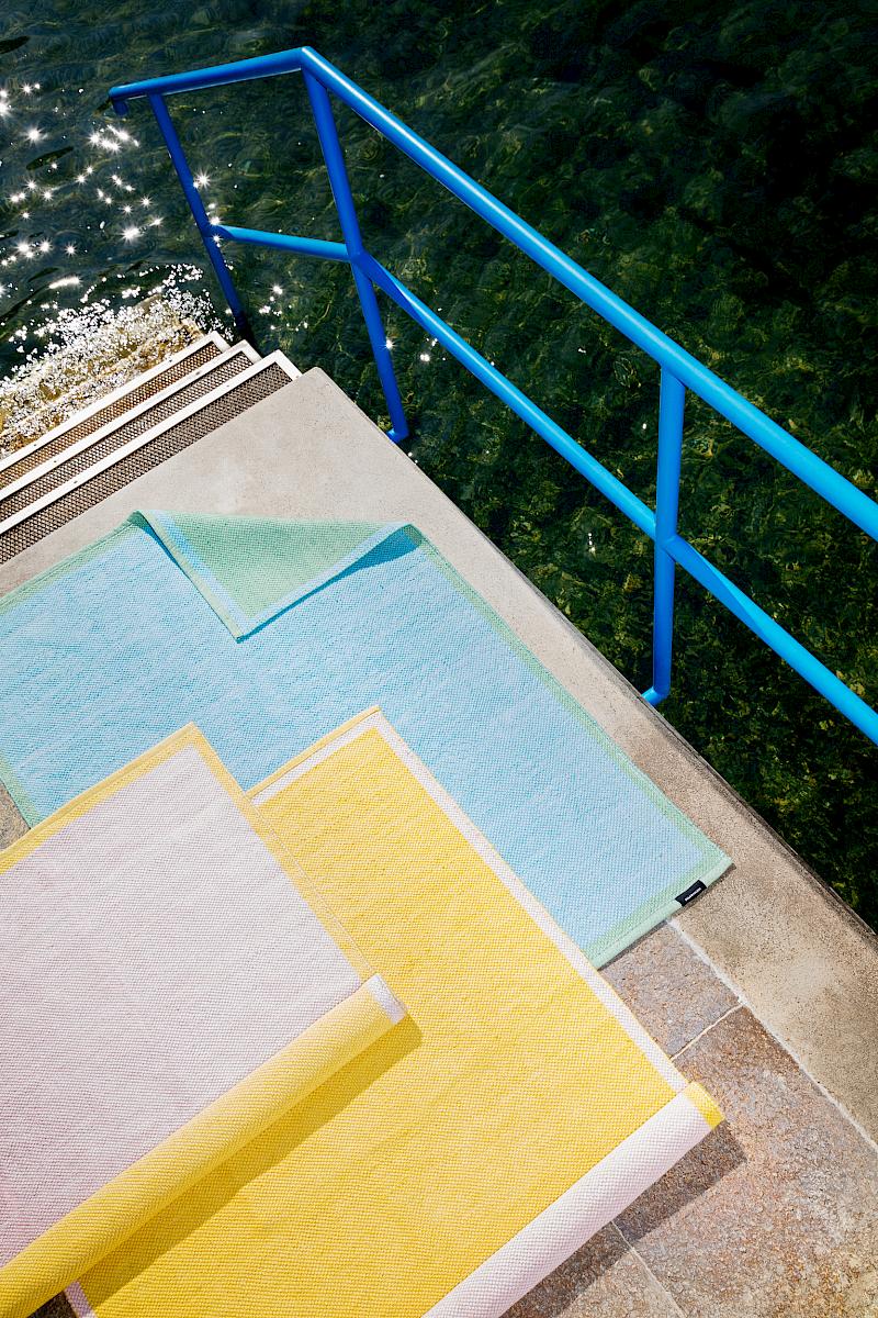 Three colourful SULA x Micasa rugs laid out neatly on a staircase leading into clear water
